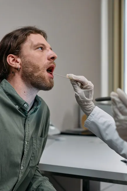 Healthcare worker administering a COVID-19 swab test to a male patient in a doctor's office.