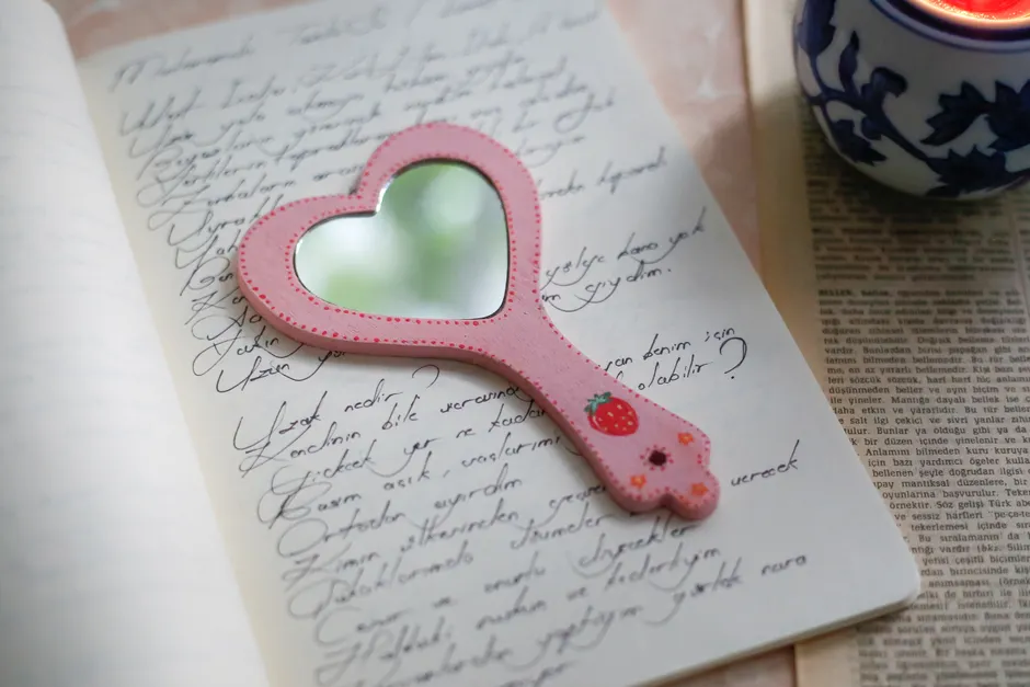Heart-shaped mirror on open notebook with handwritten text, creating a cozy reflective scene.