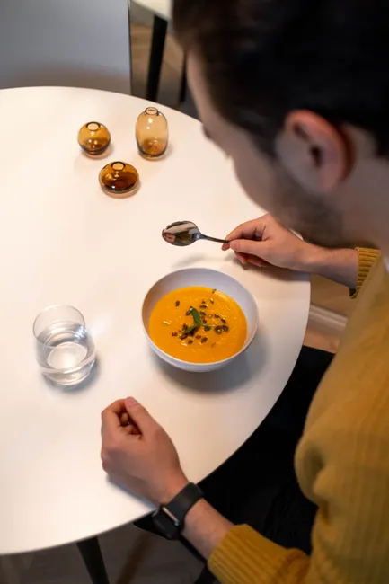 High angle view of a man eating pumpkin soup at a table indoors. Perfect for lifestyle and food themes.