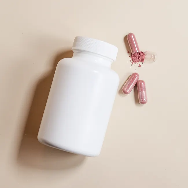 High-angle view of a white supplement bottle with pink capsules on a beige surface.