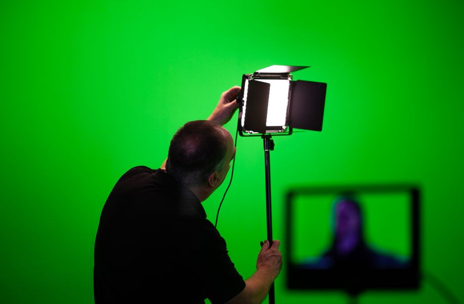 Man adjusting lighting equipment in a green screen studio setup.