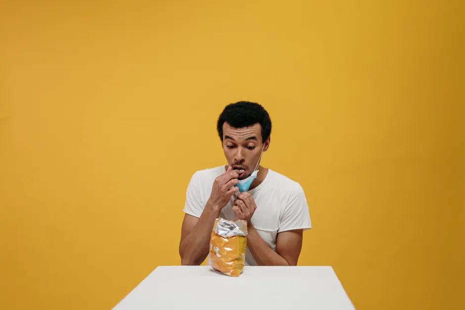Dépression et alimentation émotionnelle : comprendre le cercle sans culpabiliser Man humorously eating chips while wearing a mask in a studio setting.