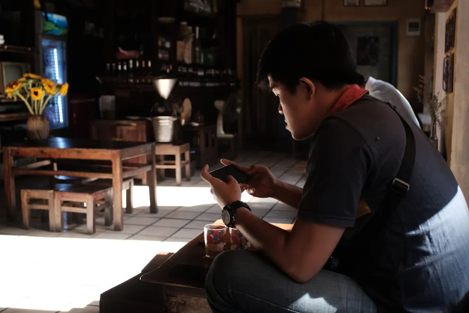 Man sitting indoors using smartphone in a rustic cafe, enjoying the tranquil atmosphere.