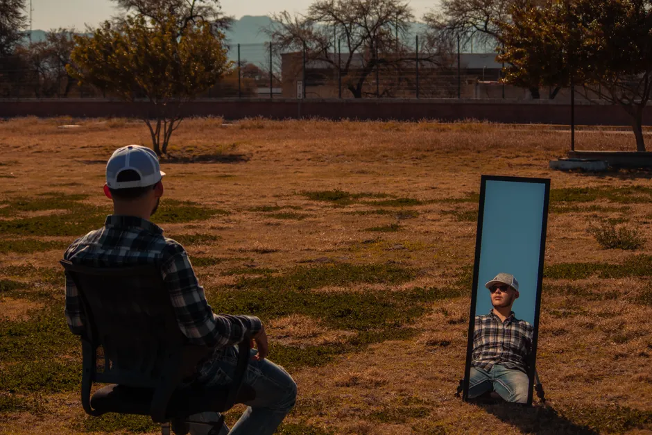 Pourquoi je me trouve moche? Comprendre l’image corporelle sans se juger Man wearing a cap sitting outdoors with reflection in a mirror, capturing a reflective moment in nature.