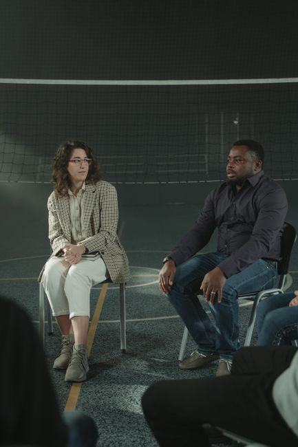 Multicultural support group in active discussion in a gym setting indoors.
