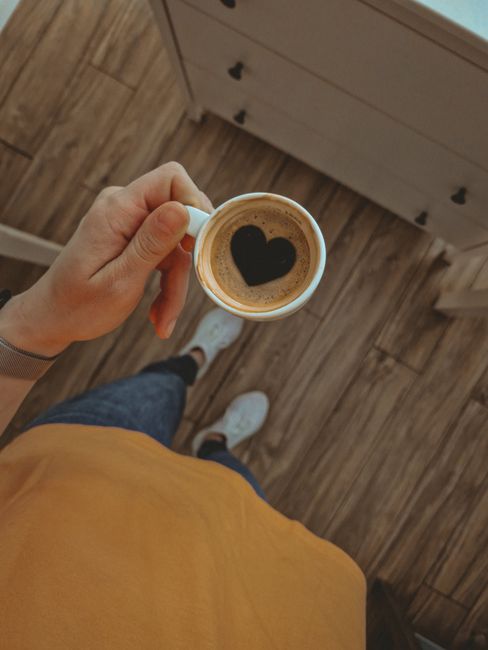 Overhead shot of a coffee cup with heart-shaped foam held by a person in a cozy setting.