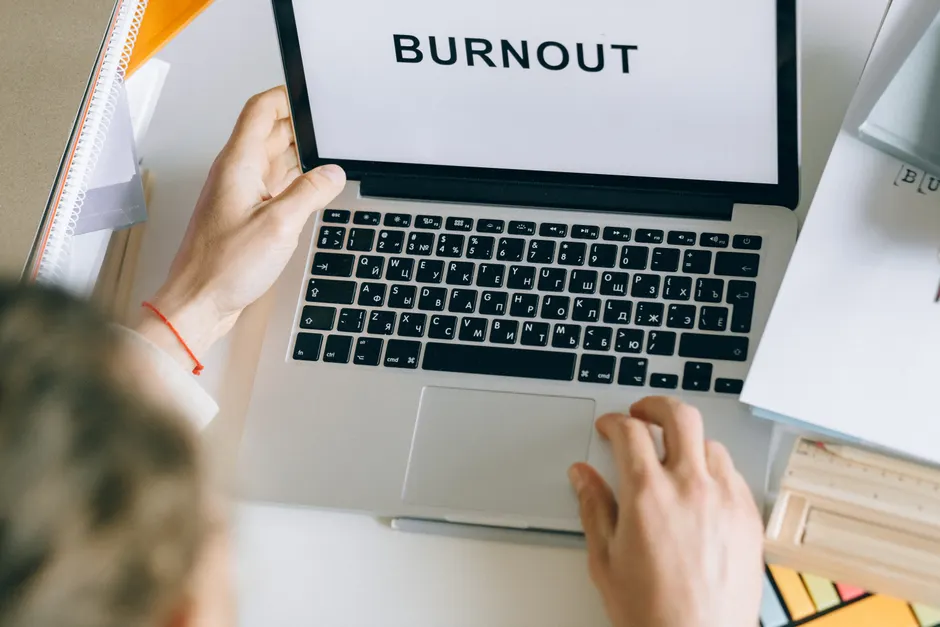 Test burnout : ce qu’un questionnaire peut, et ne peut pas dire Overhead view of a person typing 'BURNOUT' on a laptop, surrounded by office materials.