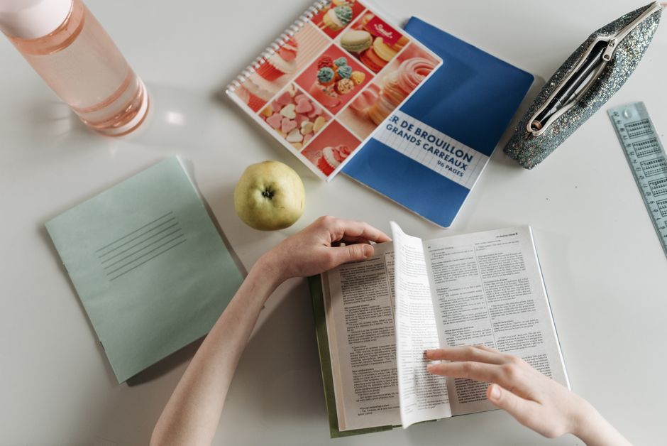 Nootropiques et TDAH : mieux se concentrer ne suffit pas à mieux apprendre Overhead view of hands turning book pages at a study desk with notebooks, apple, and water bottle.