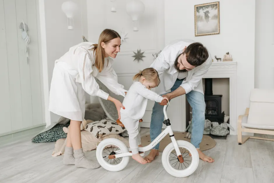 Parents assisting their child with a balance bike in a charming and cozy living room.