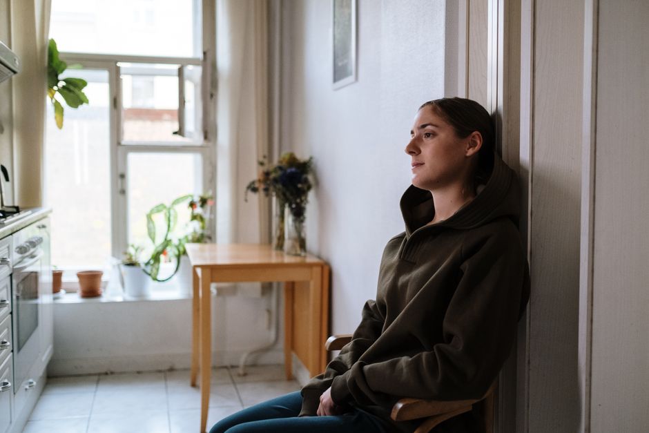 Solitude chronique : quand le manque de lien devient une souffrance durable Pensive woman in a hoodie sitting indoors by a window, capturing a moment of reflection.