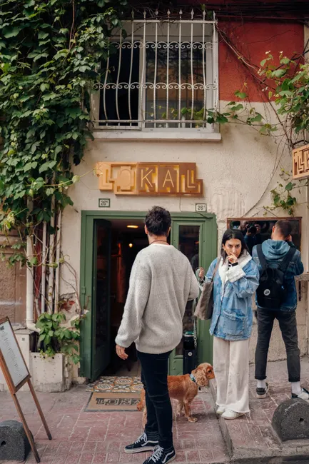 People gather outside a charming urban restaurant entrance, accompanied by a dog.