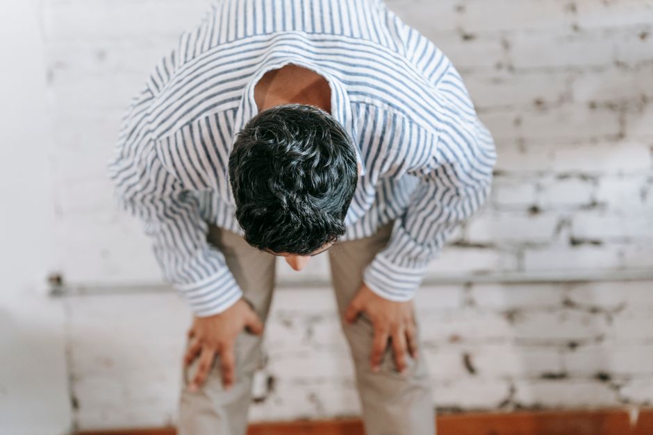 Quand le corps réagit après un traumatisme : ce que la psychologie peut dire Person in striped shirt bowing forward, posing indoors against a white brick wall.