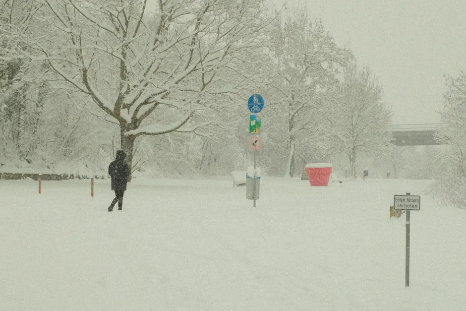 Person walking in snowy Bavarian landscape during winter with signs and trees.