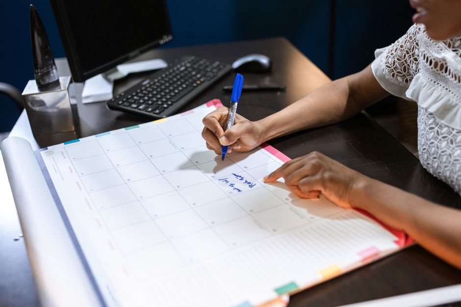 Person writing important notes in a desk calendar with a pen, set in an office.