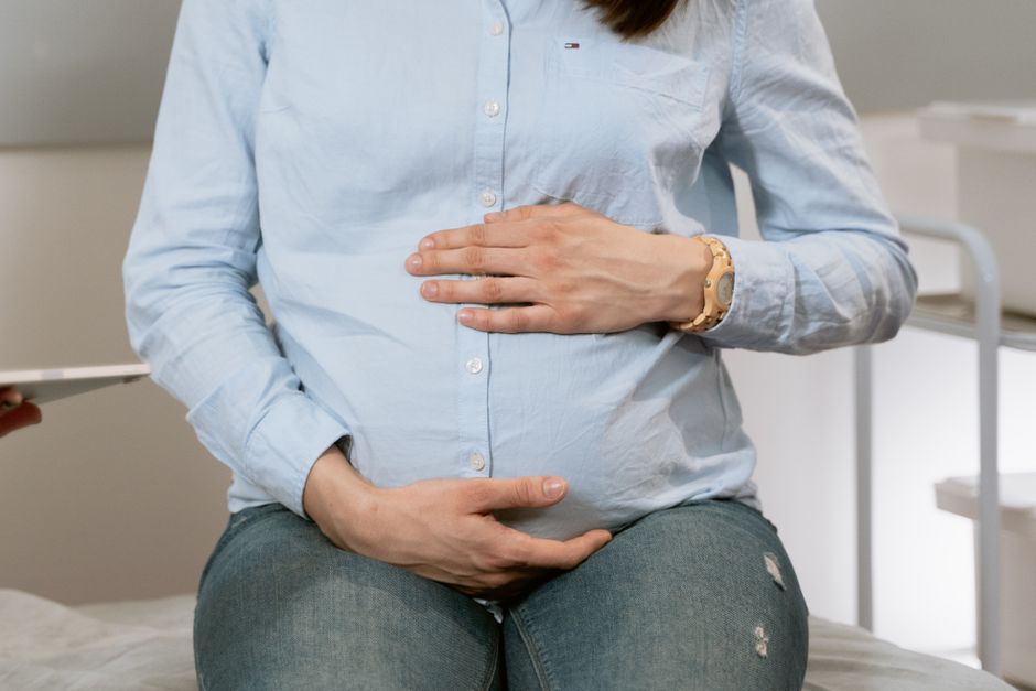 Peut-on prévenir l’autisme? Ce que la science permet d’affirmer Pregnant woman sitting indoors, hands on belly, wearing casual clothes. Healthcare consultation setting.