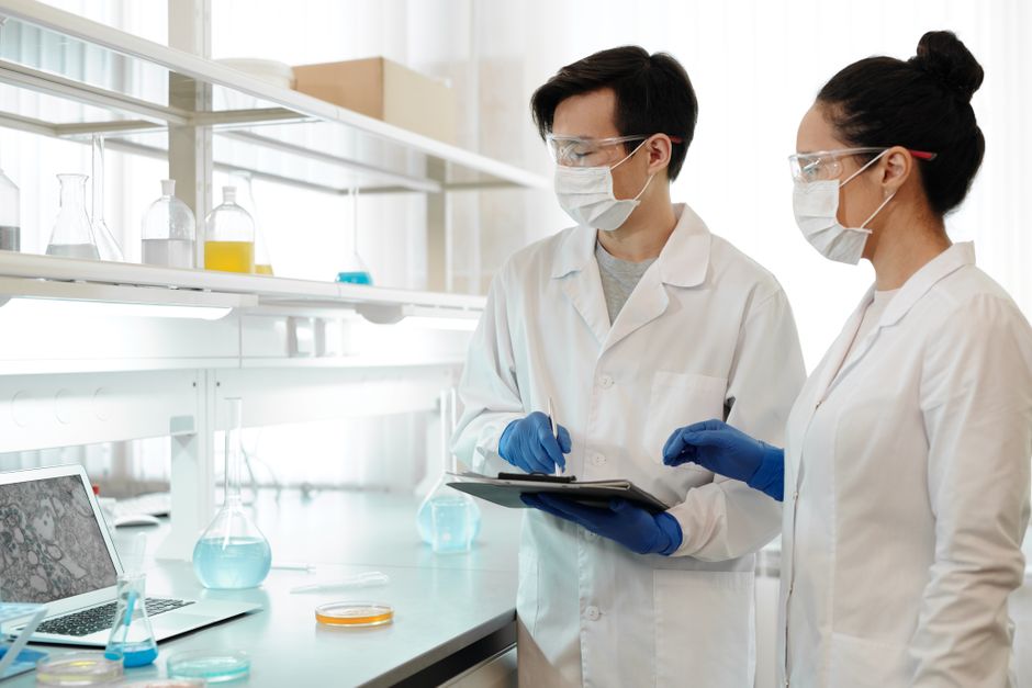 Researchers in laboratory wearing masks, gloves, and goggles working on scientific experiments.