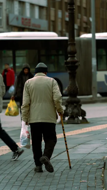 Senior adult walking with a cane on a bustling city street, embodying urban life and movement.