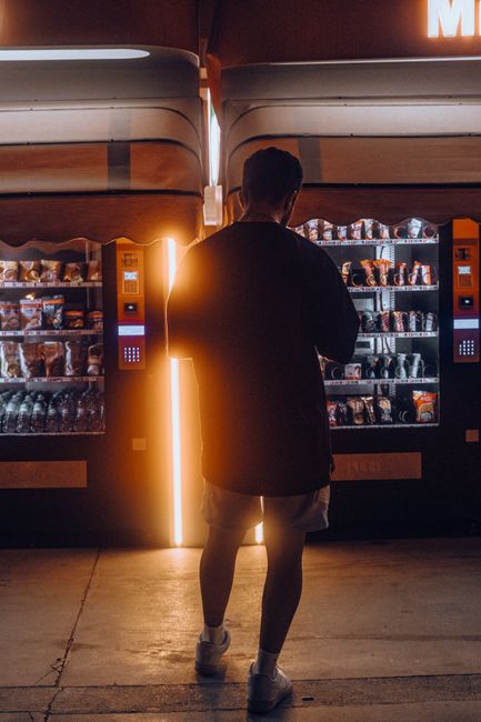 Silhouette of a man standing at illuminated vending machines during night in an urban setting.