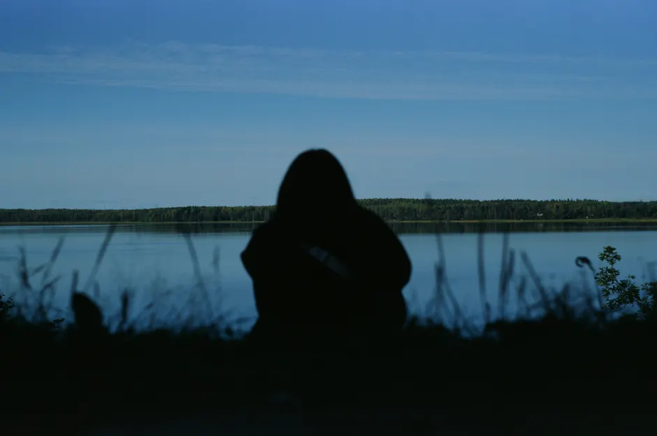 Silhouette of a person by a calm lake during a peaceful day.