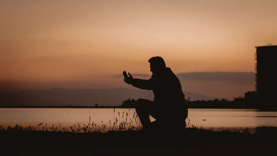 Silhouette of a person capturing a sunset by the water in Amsterdam with a smartphone.