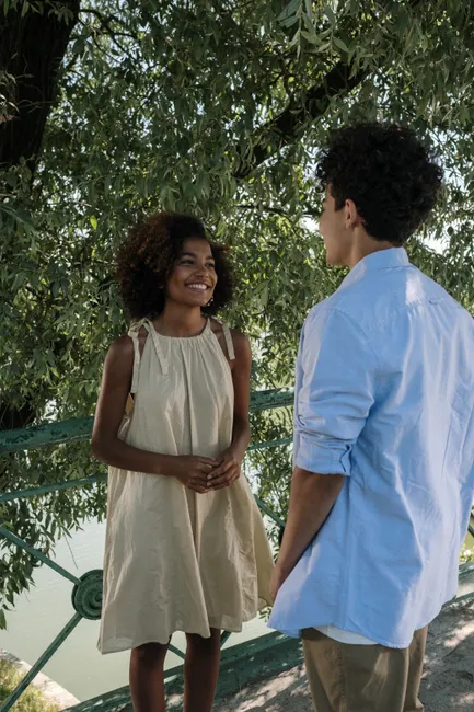 Smiling couple chatting under a tree in a sunny outdoor park setting.