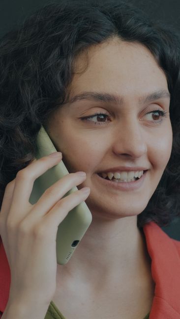 Smiling young woman talking on a smartphone indoors, wearing a pink and green outfit.