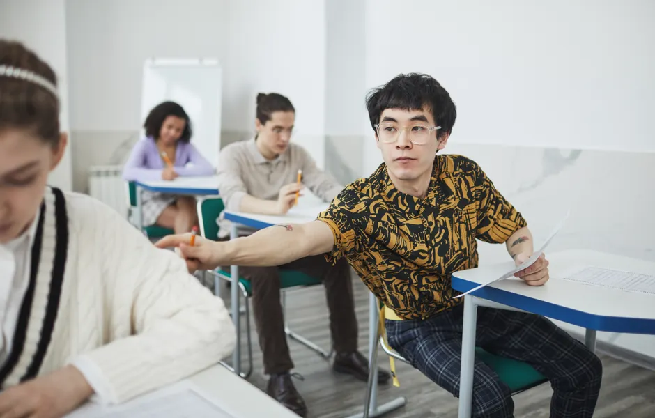 Students engaged in an exam setting, one attempting to view a classmate's paper. High school classroom scene.