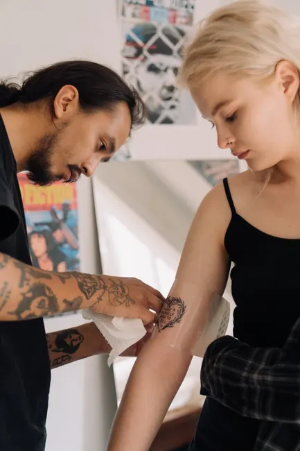 Tattoo artist carefully wraps a fresh tattoo on a young woman's arm in a studio setting.