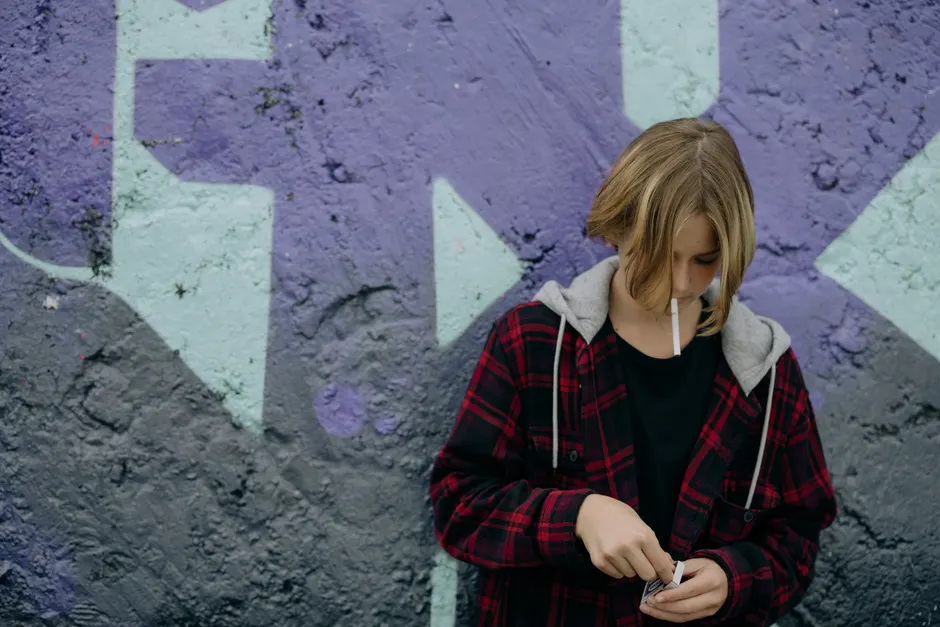 Vapotage et santé mentale : dépression, anxiété et dépendance Teenager in a checked jacket holding a cigarette by a graffiti wall, illustrating urban youth culture.