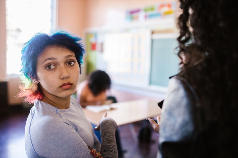 Teenager with vivid dyed hair in a classroom environment, observing the lesson.