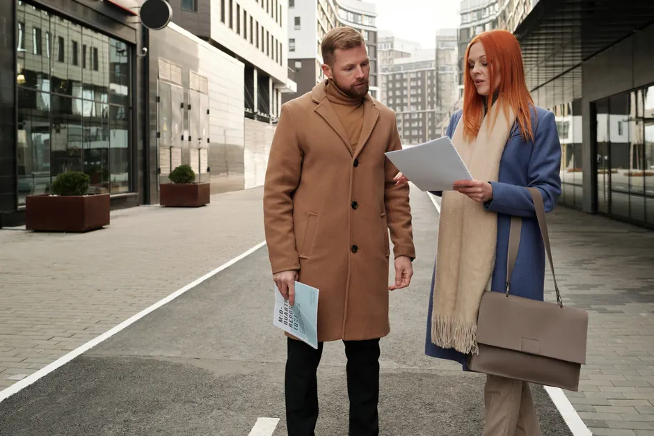 Two business professionals discussing documents on a city street. Collaboration and partnership in an urban setting.