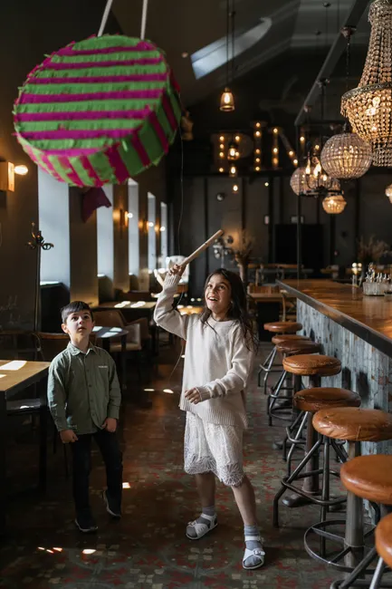 Two children enjoying a fun piñata activity in a warmly lit, cozy cafe setting.