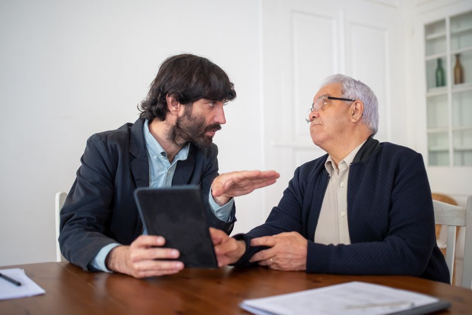 Two men having a professional discussion with a digital tablet at a wooden table indoors.
