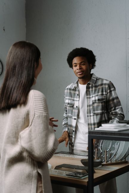 Two people in a stylish, modern room engaged in conversation, showcasing contemporary fashion.