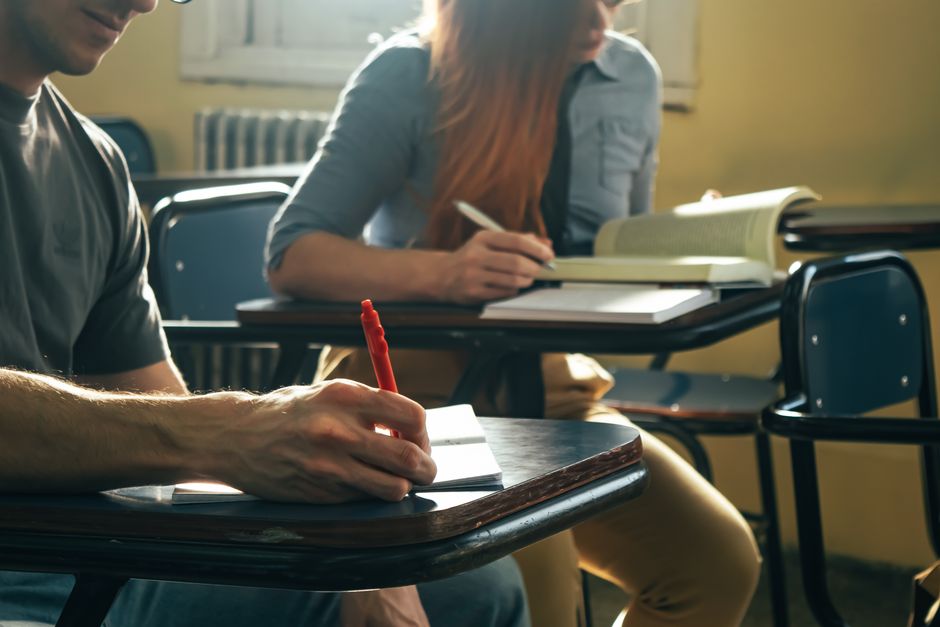 Two students engage in note-taking and reading during class, highlighting study focus and education.