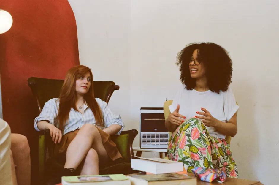Two women engaged in a casual discussion in a cozy indoor setting.