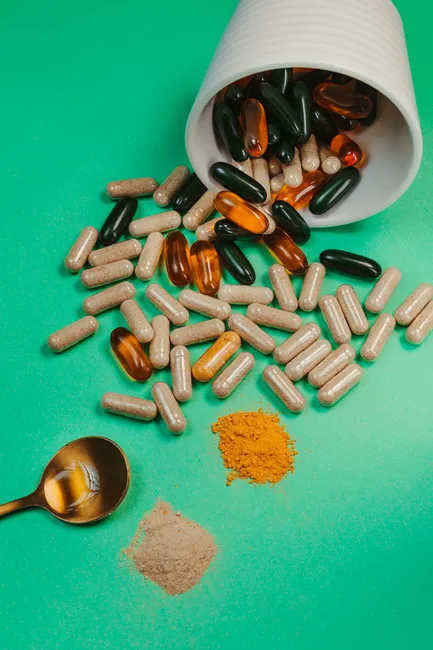 Variety of capsules and powders with a spoon on green backdrop. Ideal for health and wellness themes.