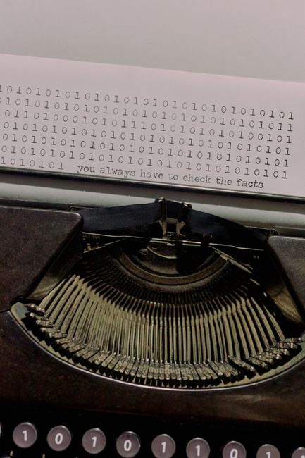 Vintage typewriter typing binary code with a quote about fact-checking.